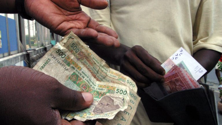 Dos hombres intercambian billetes de francos CFA. Foto: Thierry Guegnon PW/SM.