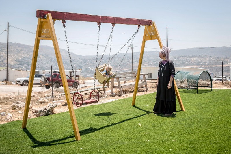 Una colona israelí balancea a uno de sus hijos en los columpios instalados en el asentamiento de Evyatar